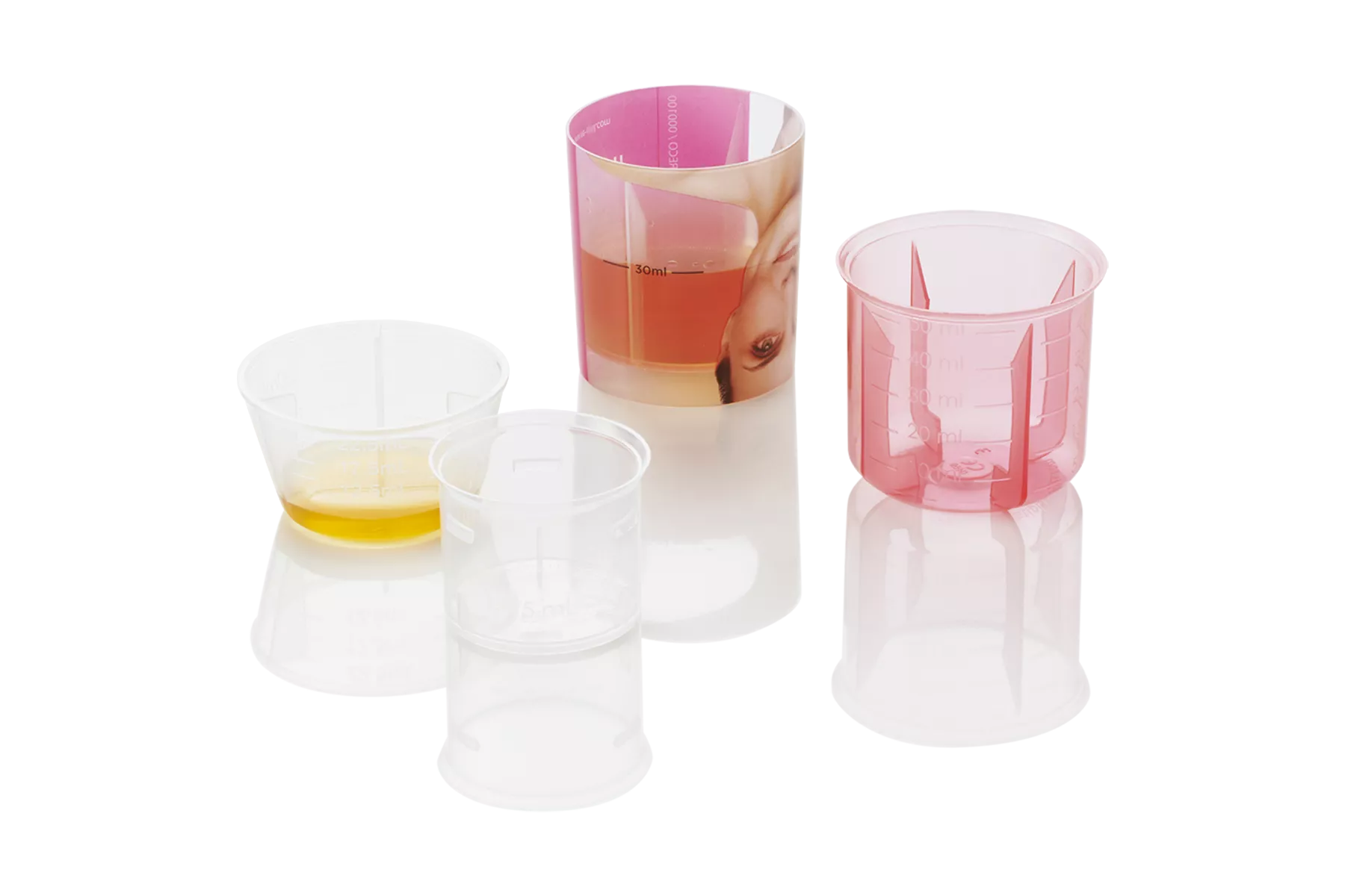 Composition of measuring cups: cup with IML printing and liquid inside, transparent pink cup, transparent cups with and without liquid inside.