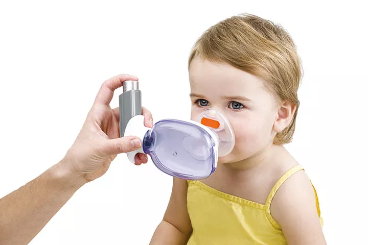 An adult holds the inhaler in his hand and administers the medicine to a little girl